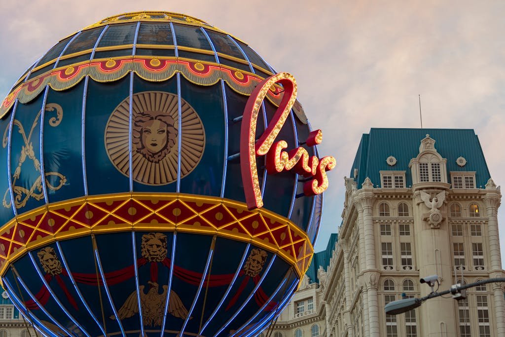 Illuminated Paris Hotel sign with ornate globe on cloudy evening in Las Vegas.