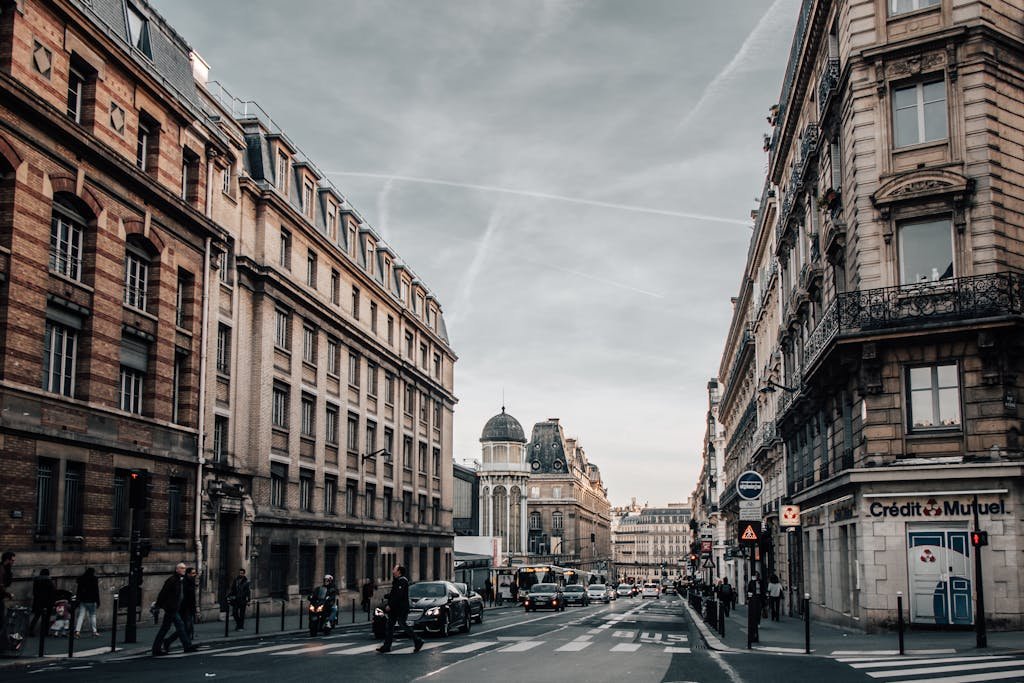 Urban street scene in Paris with classic architecture, cars, and pedestrians on an overcast day.