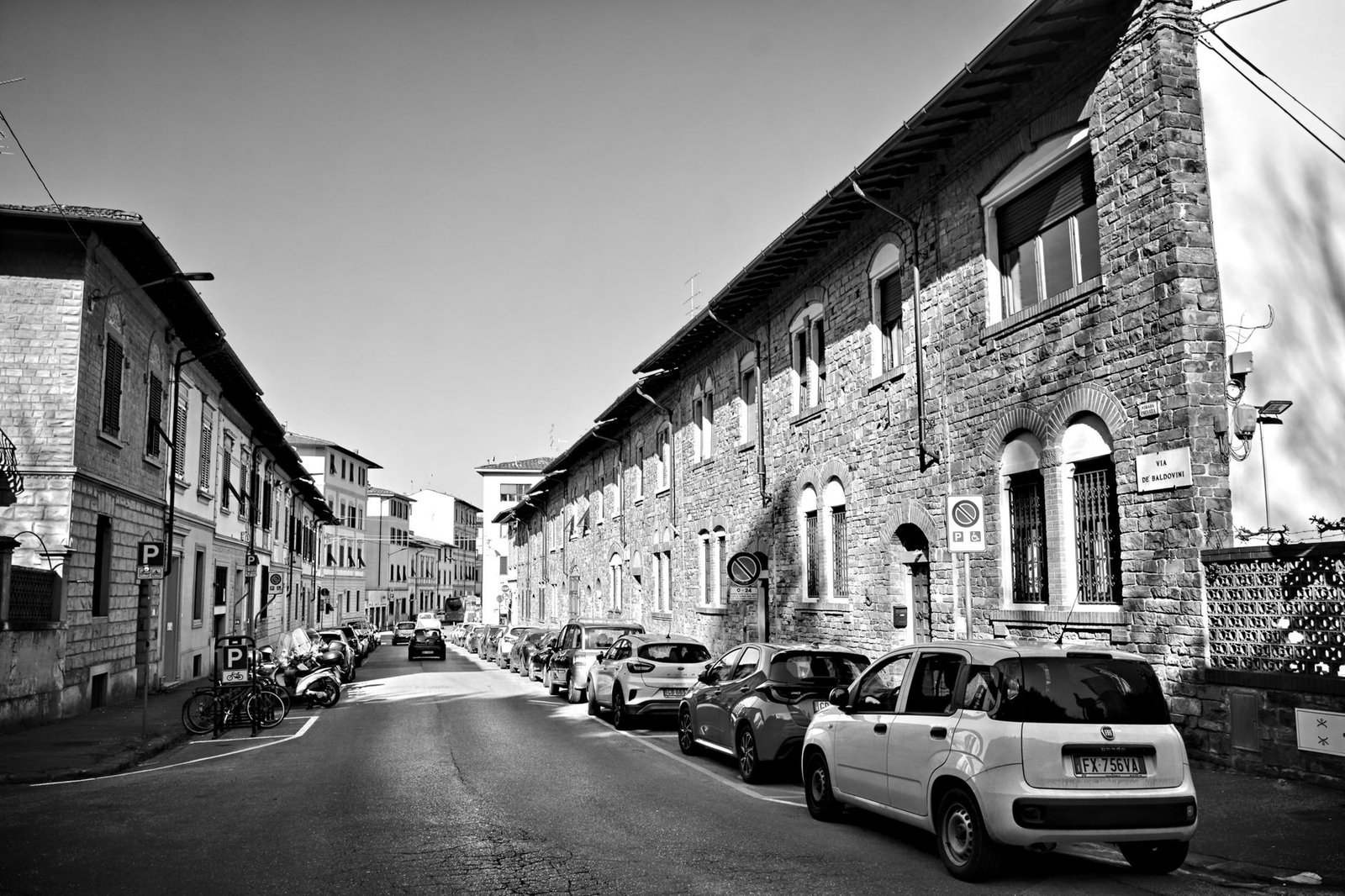 Escena de una calle europea con coches aparcados y edificios históricos, en blanco y negro