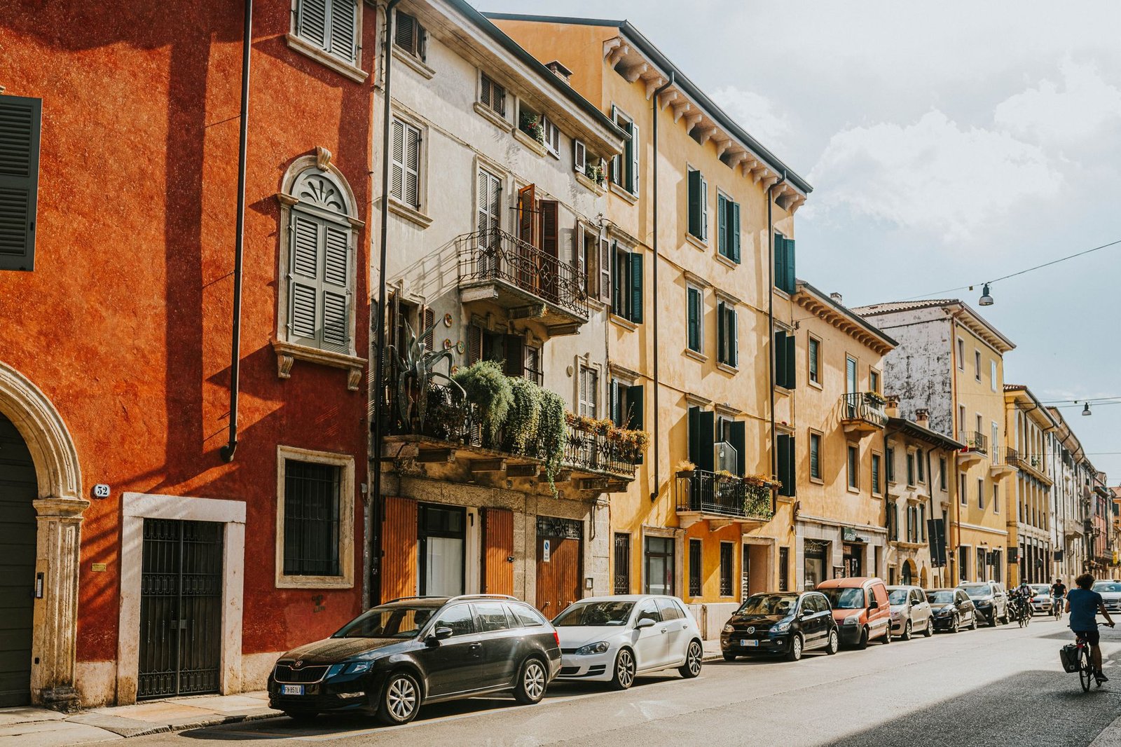 Edificios históricos de colores y coches aparcados en una calle soleada de Verona, Italia